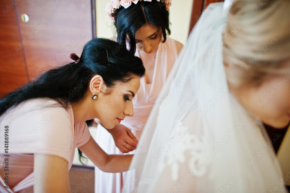 Naklejka premium Fashionable bridesmaids on pink dresses helped wear bow on back of wedding dress bride. Morning wedding day.