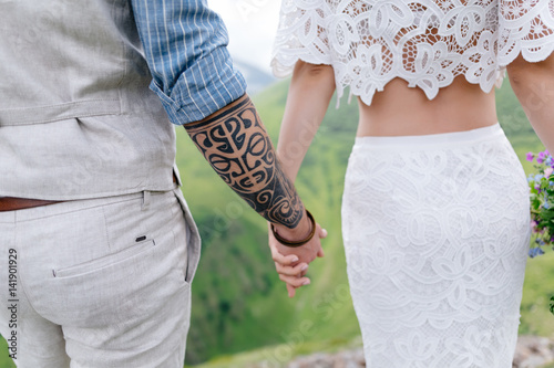 Rear view of a young couple in love, holding hands and enjoying beautiful scenery on mountains