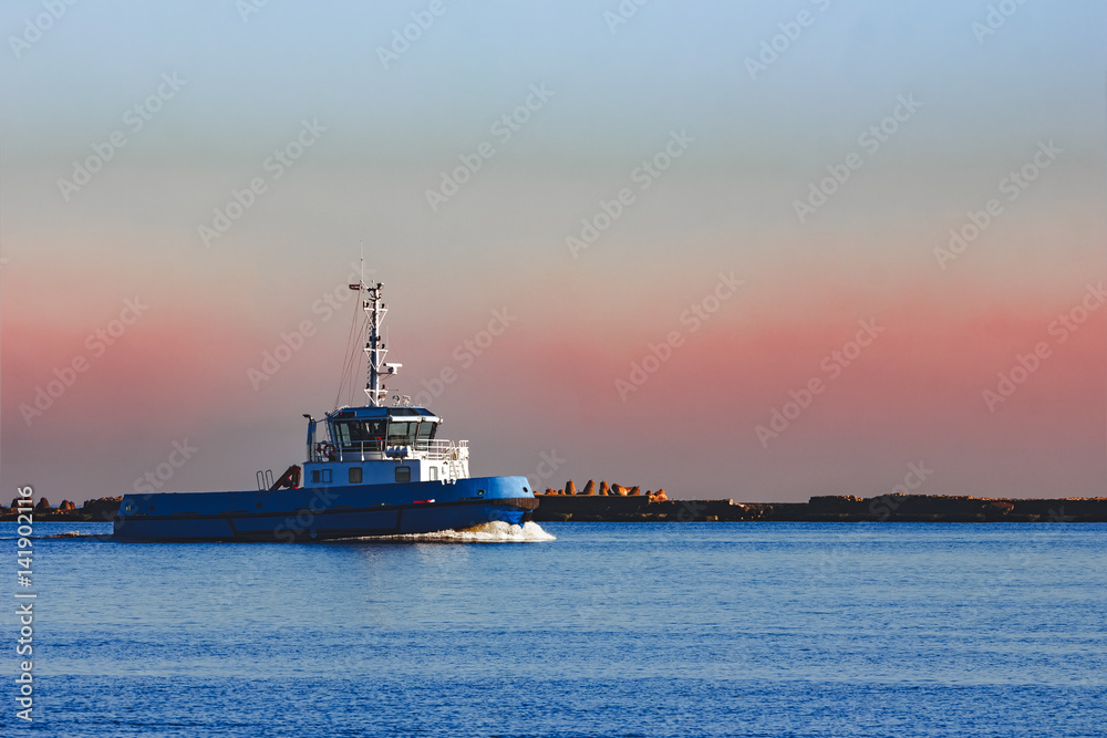 Fototapeta premium Blue small tug ship sailing past the breakwater dam in morning