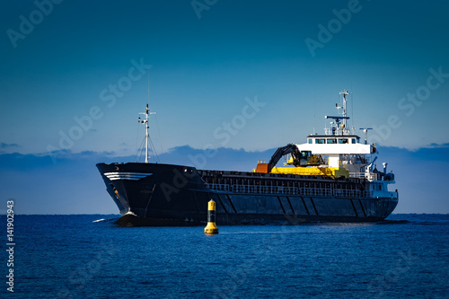 Black cargo ship with long reach excavator moving by baltic sea