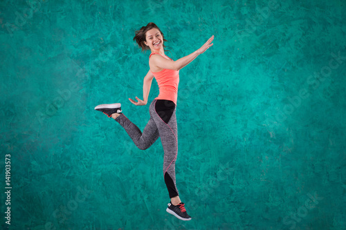 Sport young female in fashion sportswear jumping over turquoise background.