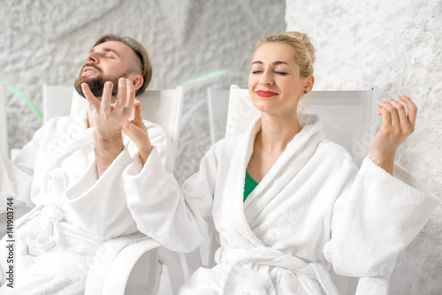 Young couple in bathrobes meditating in the salt room