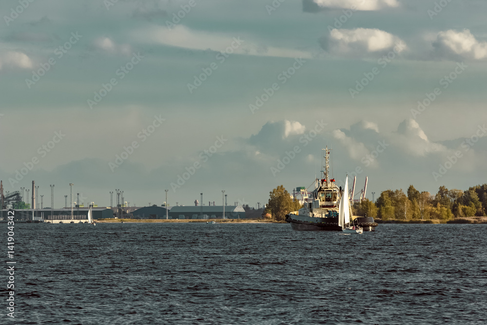 Tug ship and sailboat are coming to port of Riga, Daugava river