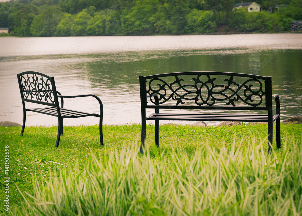Decorative metal park benchs overlooking still water. Decorative metal park benchs overlooking still water.