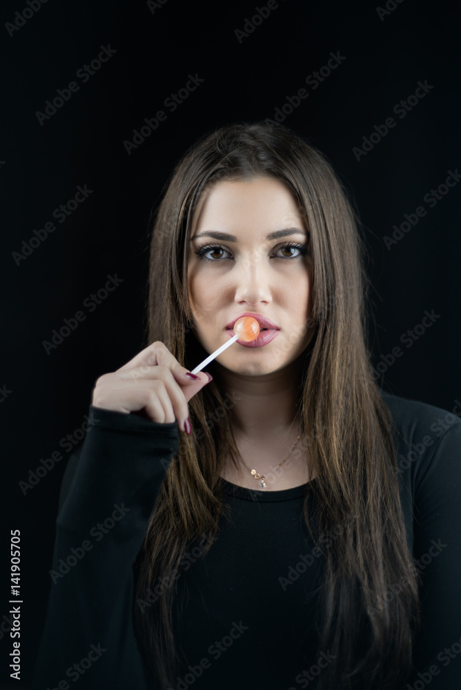 Young woman touching a lollipop on her juicy big lips, wear a black blouse,isolated black background Young woman touching a lollipop on her juicy big lips, wear a black blouse,isolated black background