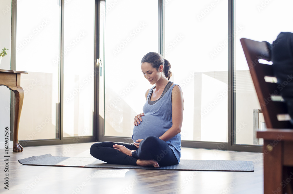 Pregnant woman holding abdomen while sitting on exercise mat at home