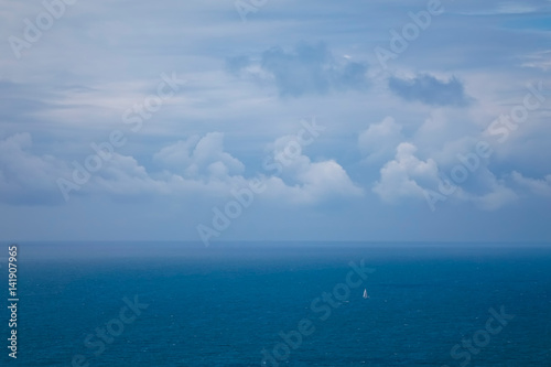 Small, White Sailboat on the Ocean under a Cloudy Sky