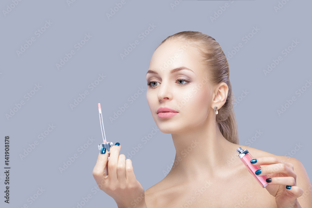 Obraz premium beautiful blond woman holding pink lip gloss on gray background. lip makeup