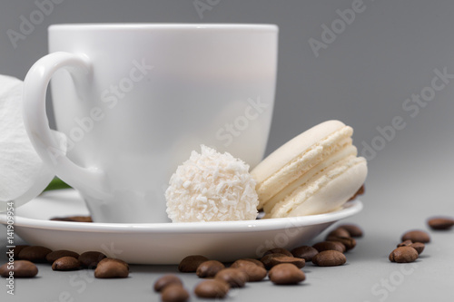 White cup of coffee with candy on a gray background