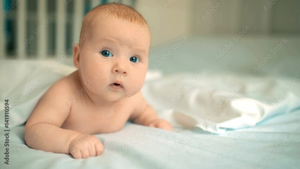Cute baby with beautiful blue eyes lying in white bed Cute baby with beautiful blue eyes lying in white bed