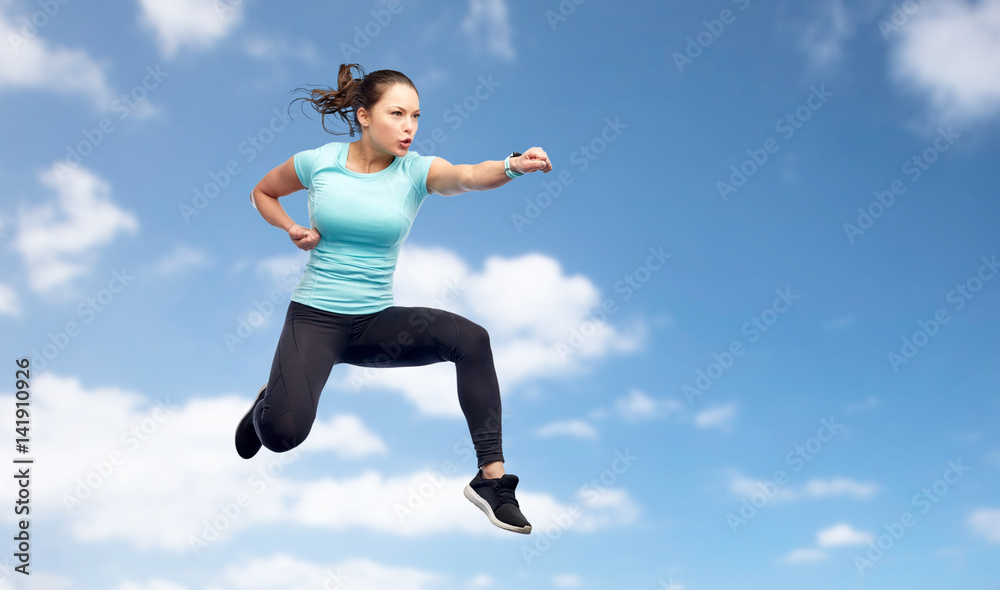 sporty woman jumping in fighting pose over sky