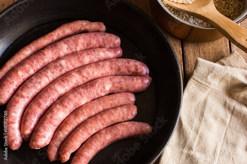 Raw sausages in iron cast pan, rice in copper pot, linen towel on wood kitchen table, top view, cooking concept, photo