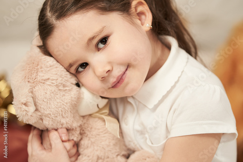 Portrait of expressive little girl hugging her plush bear friend, indoor shot. Little girl playing with teddy bear