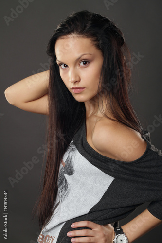 Beautiful girl in a long T-shirt posing on gray background.