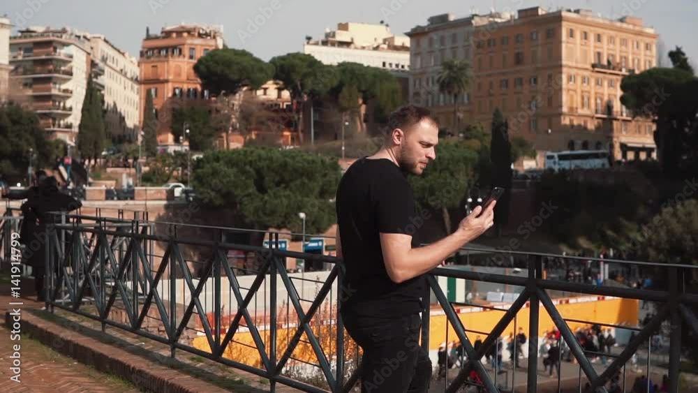 Middle-aged handsome man watches pictures, takes photo in Rome, Italy, smiling, exploring new city. Slow motion.