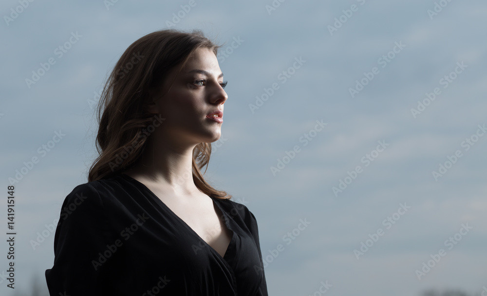 Beautiful woman in black dress against sullen sky background Beautiful woman in black dress against sullen sky background