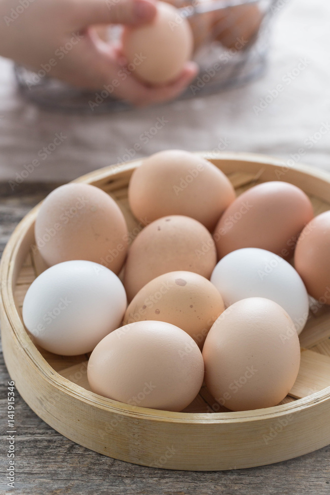 Farm fresh eggs in a bamboo basket. Female hands and more eggs in the background. Farm fresh eggs in a bamboo basket. Female hands and more eggs in the background.