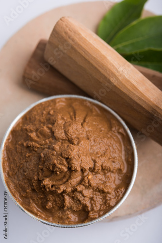 Ayurvedic Chandan powder or sandalwood paste in silver bowl with sticks and leaves placed over sahan or sahana or circular stone base for creating paste photo