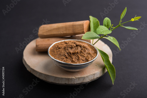 Ayurvedic Chandan powder or sandalwood paste in silver bowl with sticks and leaves placed over sahan or sahana or circular stone base for creating paste photo