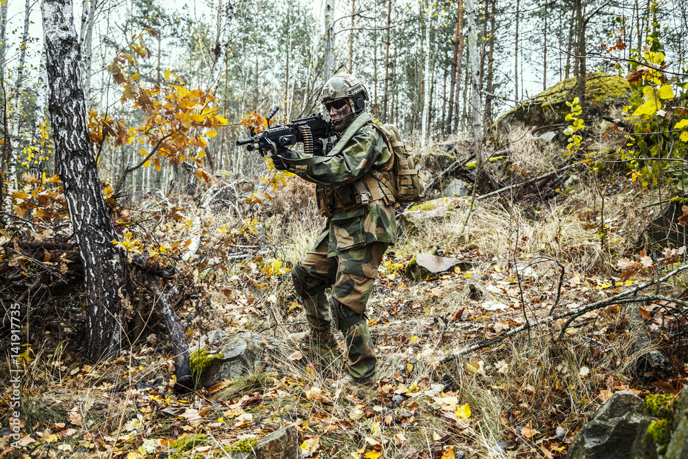 Norwegian Rapid reaction special forces FSK soldier patrolling in the forest. Field camo uniforms, knee pads, combat helmet and eye-wear goggles are on