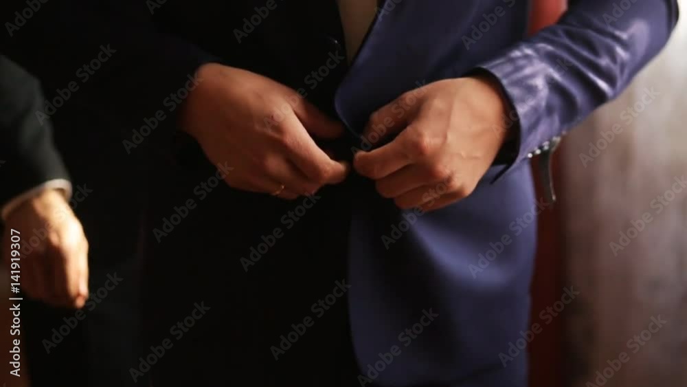 Groom buttoning up his dark blue jacket before wedding ceremony. Close up. Soft light