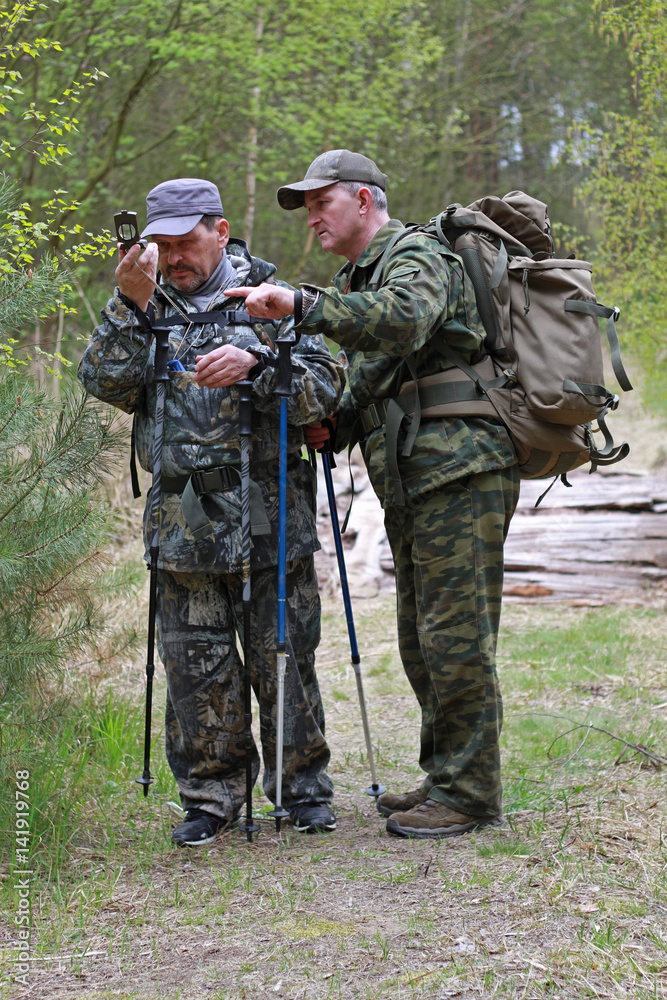Two men in camouflage uniforms and backpacks to define your way across the map using a compass. Two men in camouflage uniforms and backpacks to define your way across the map using a compass.