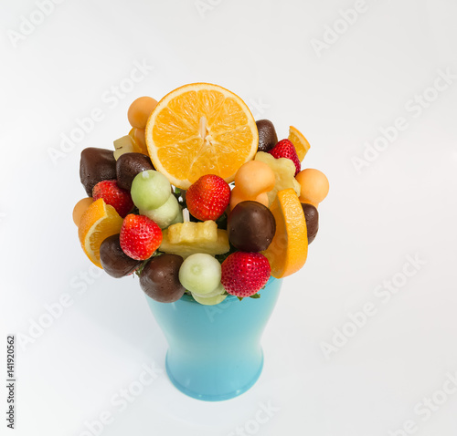 beautiful closeup view of assorted various natural appetizing fruits mixed with dark chocolate bouquet in ceramic blue vase on white grayish background