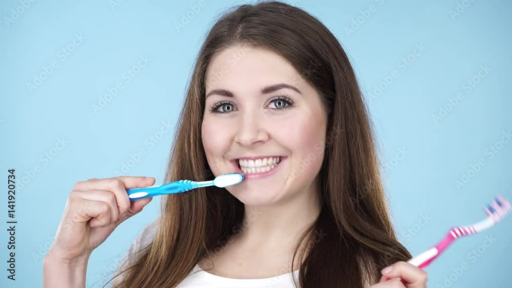 Woman holding two brushes for teeth cleaning. Happy positive smiling girl with toothbrush. Oral daily hygiene. Studio shot on blue background 4K ProRes HQ codec Woman holding two brushes for teeth cleaning. Happy positive smiling girl with toothbrush. Oral daily hygiene. Studio shot on blue background 4K ProRes HQ codec