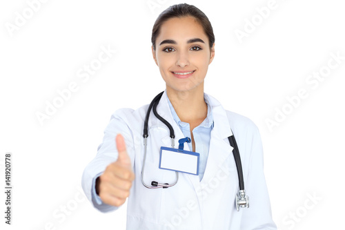 Cheerful smiling female doctor showing thumbs up  isolated over white background. Latin american or Hispanic young woman