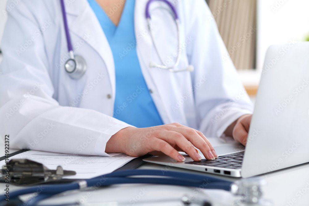 Close up of unknown female doctor typing on laptop computer while sitting at the table. Medical staff, compulsory work concept Close up of unknown female doctor typing on laptop computer while sitting at the table. Medical staff, compulsory work concept