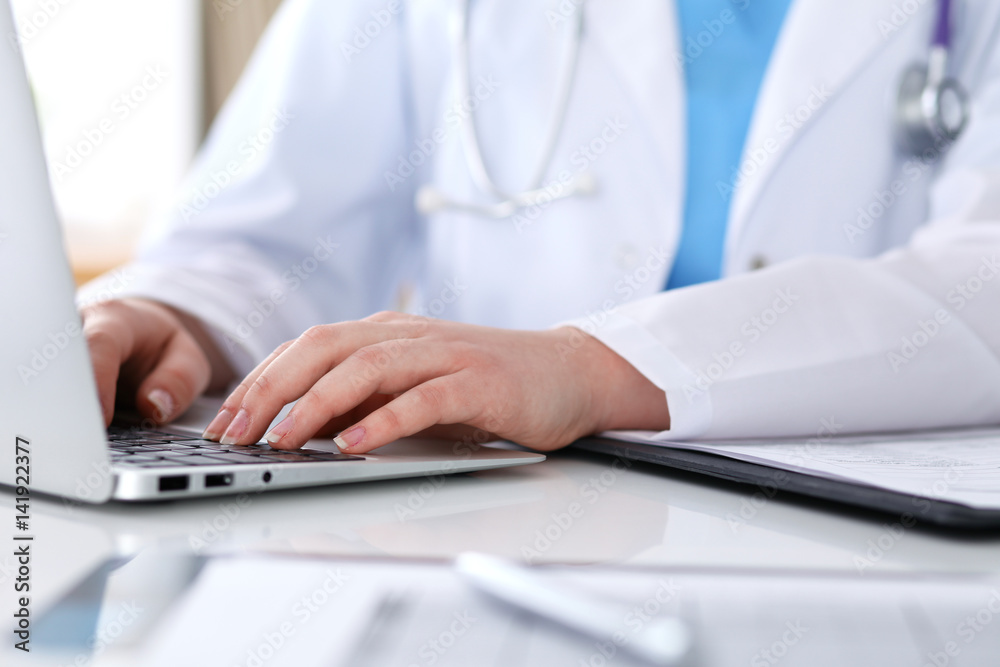 Close up of unknown female doctor typing on laptop computer while sitting at the table. Medical staff, compulsory work concept Close up of unknown female doctor typing on laptop computer while sitting at the table. Medical staff, compulsory work concept