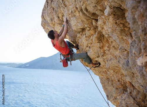 Young man struggling to climb overhanging cliff