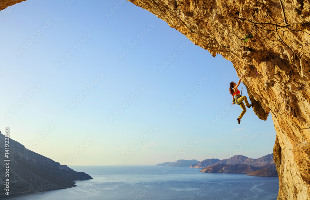 Young woman climbing challenging route in cave at sunset - obrazy, fototapety, plakaty 