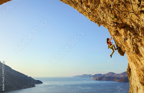 Young woman climbing challenging route in cave at sunset