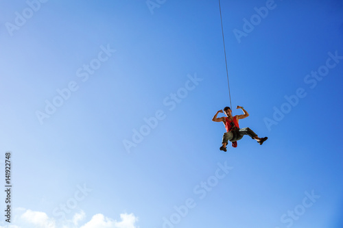 Rock climber swinging on rope and flexing muscles
