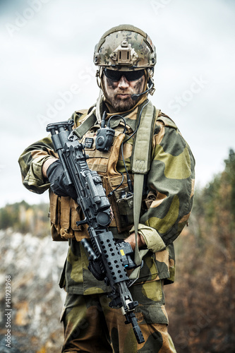 Norwegian Rapid reaction special forces FSK soldier patrolling in the forest. Painted face, combat helmet and eye-wear goggles are on