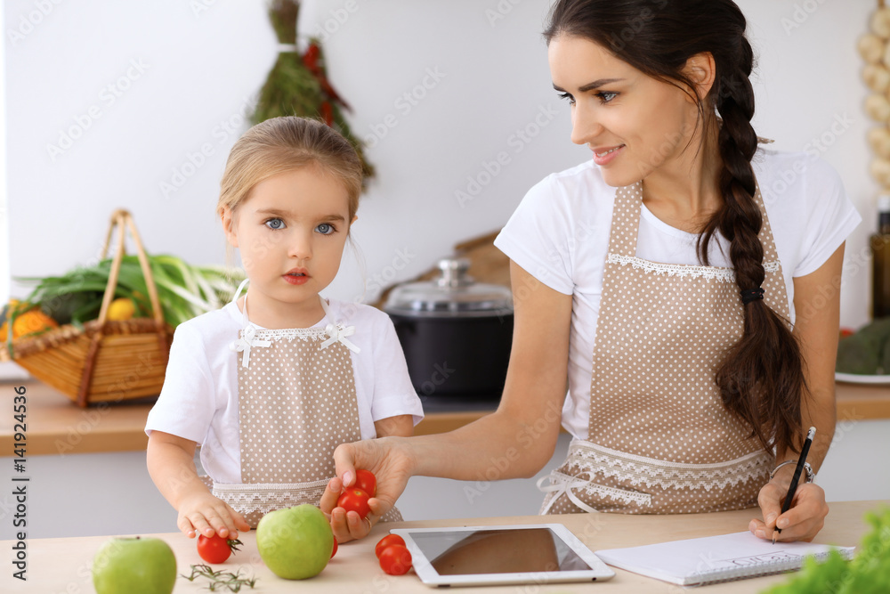 Happy family in the kitchen. Mother and child daughter make menu for cooking tasty breakfast in the kitchen Happy family in the kitchen. Mother and child daughter make menu for cooking tasty breakfast in the kitchen