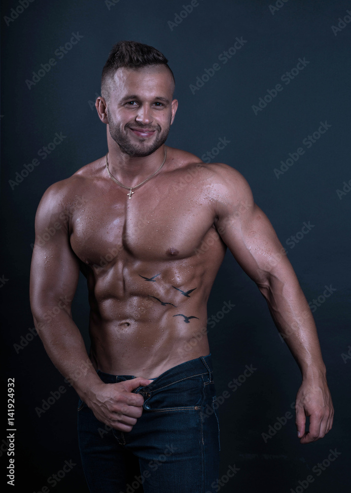 Happy smiling sexy handsome shirtless fitness model bodybuilder shows his perfect muscular body