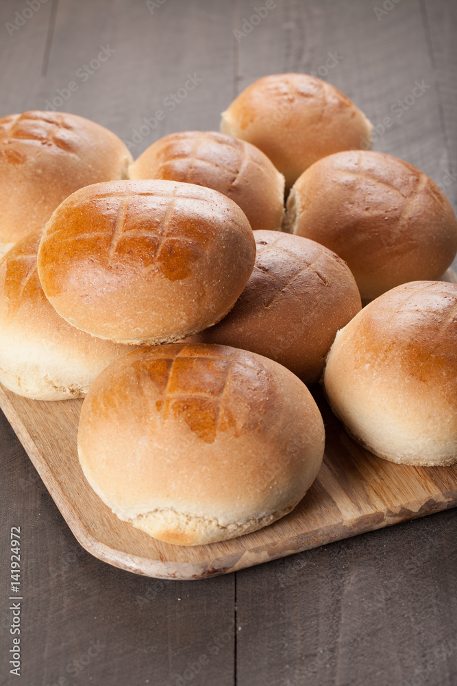 Large Baked Homemade Rolls stacked on cutting board on dark wooden background vertical shot
