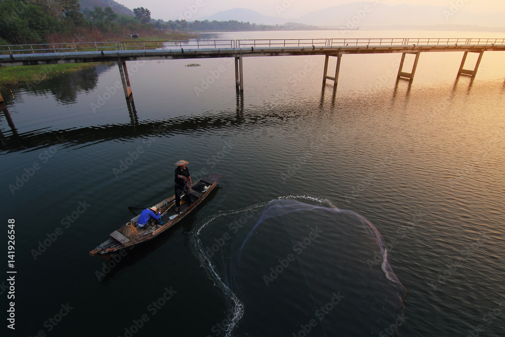 Asian fishermen using nets to catch fish at the Bangpra lake with beautiful scenery of nature during sunrise time. Bang Pra Reservoir at Chonburi province in Thailand