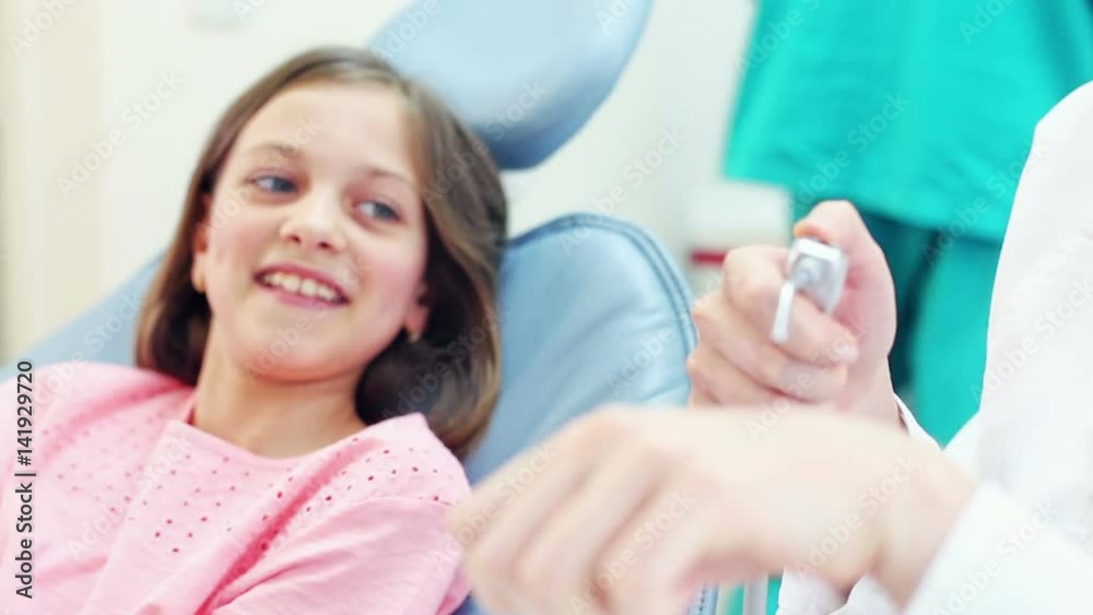 Young female dentist showing dental instruments to a little girl, playing with instruments, graded