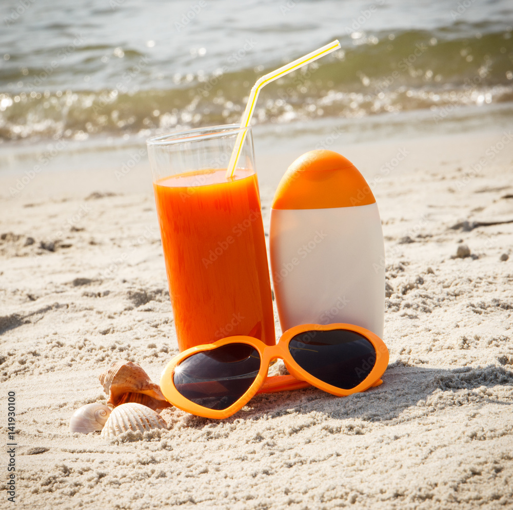 Carrot juice, sunglasses and sun lotion at beach, concept of vitamin A and beautiful, lasting tan
