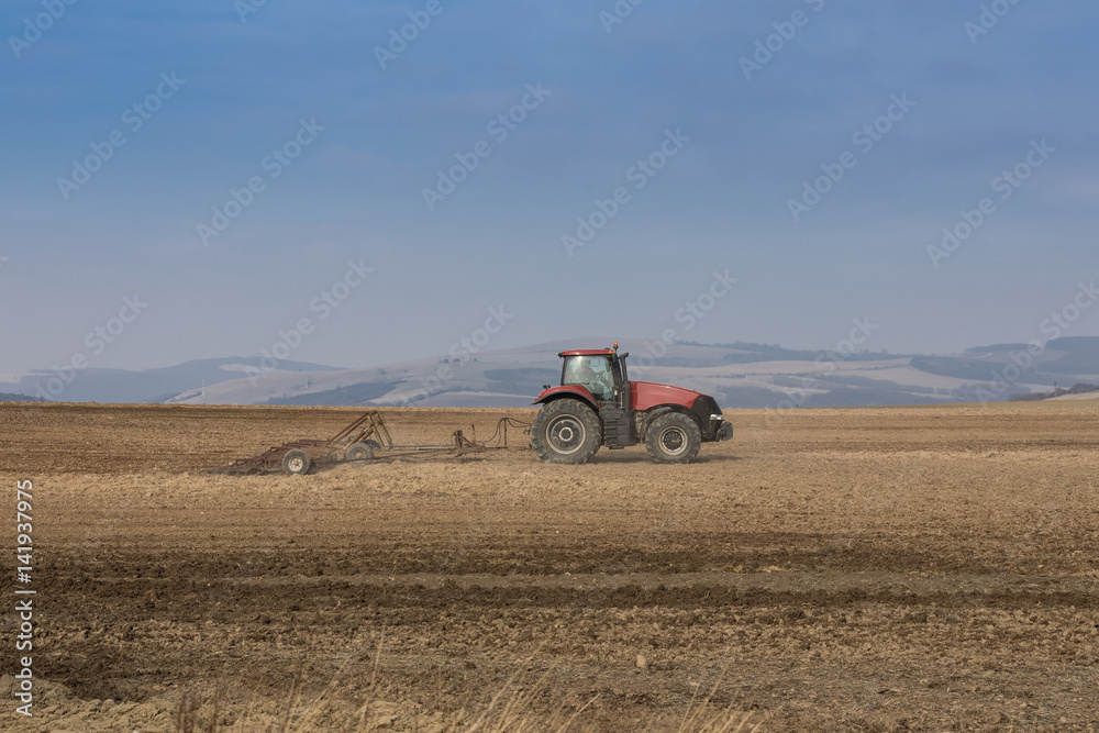 Obraz premium red modern tractor raking soil , land management