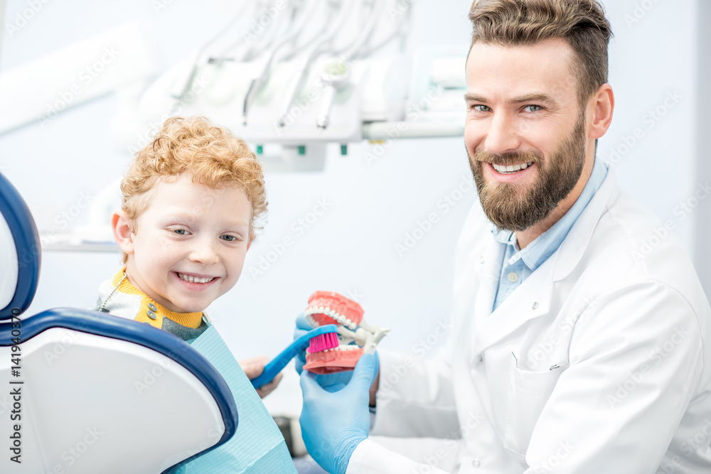 Fototapeta premium Dentist showing the boy how to brush teeth on artificial jaw at the dental office