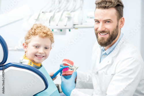 Dentist showing the boy how to brush teeth on artificial jaw at the dental office