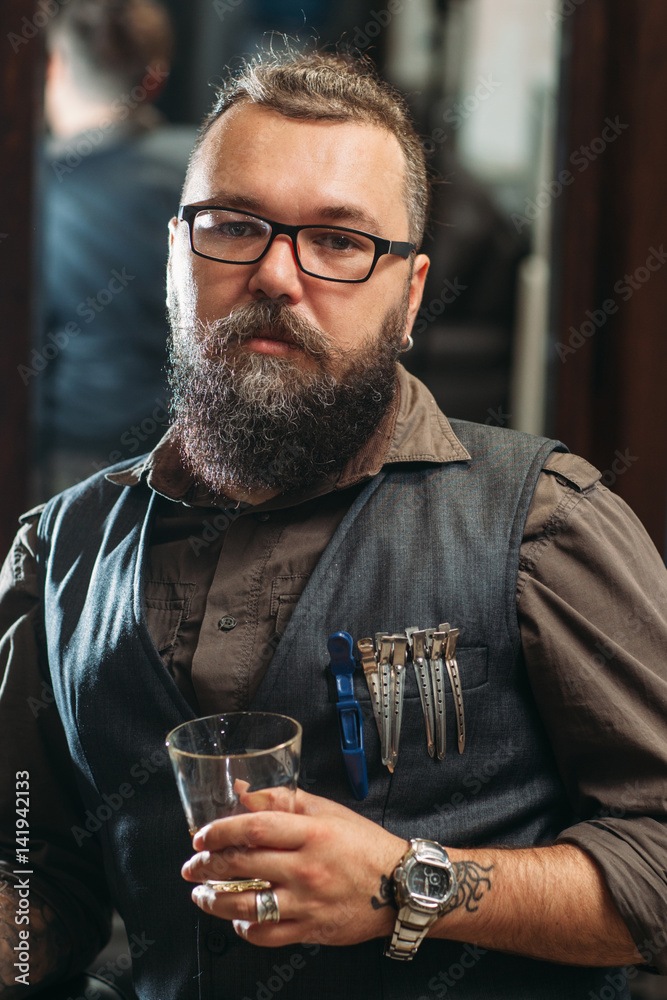 Brutal biker looking at camera with whiskey. Portrait of senior bearded man in leather shirt posing posing with glass in hand. Lifestyle, hobby, rock concept Brutal biker looking at camera with whiskey. Portrait of senior bearded man in leather shirt posing posing with glass in hand. Lifestyle, hobby, rock concept