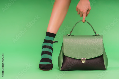 Two-colored photo: green and black handbag and woman's hand holding it on a green background. 