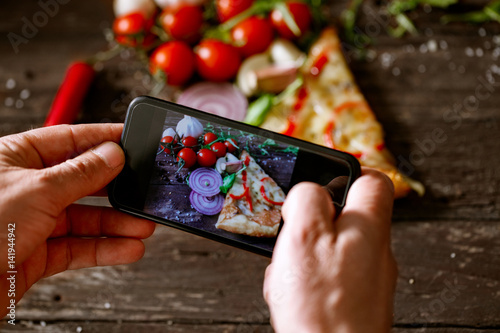 man using smartphone to take picture of slice of pizza.