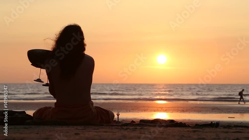 GOA, INDIA - 21 JANUARY 2015: Man sitting on beach at sunset playing music to the sun. photo