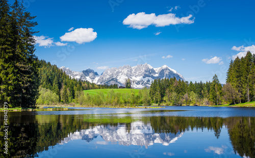 Snowy mountain range is reflected in a small lake near Kitzbuehel, Tyrol, Austria